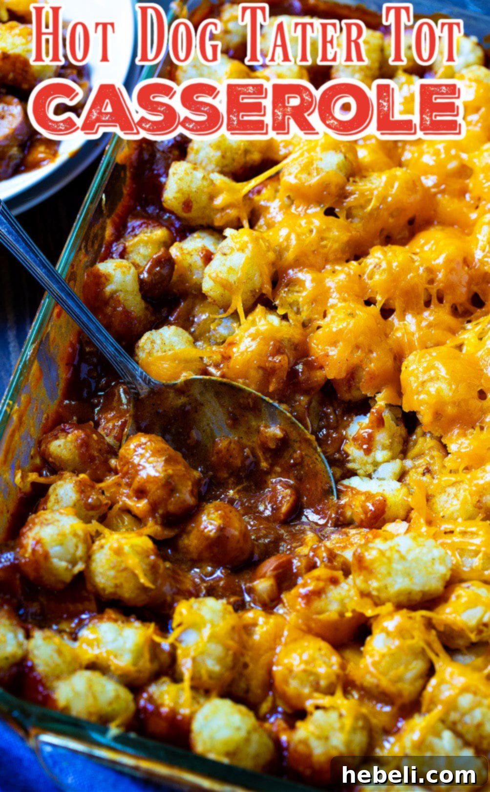 A serving spoon dishing up a generous portion of Cheesy Hot Dog Tater Tot Casserole.