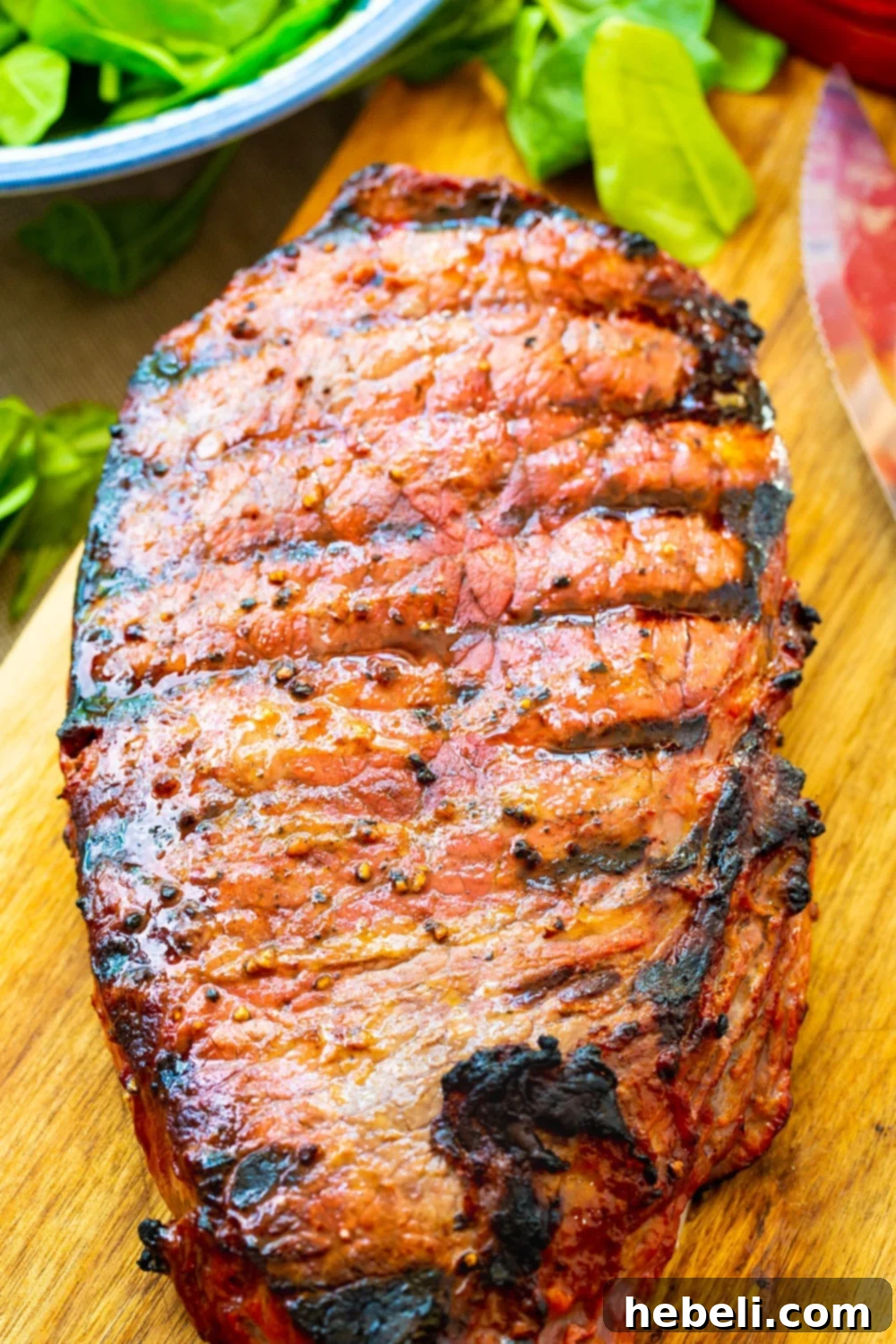 A whole grilled London Broil steak resting on a cutting board, showcasing its caramelized exterior.