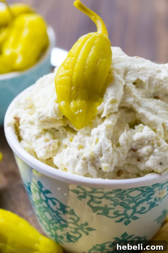 Three Cheese Pepperoncini Spread in a rustic bowl, surrounded by an array of crunchy crackers and fresh crudités.