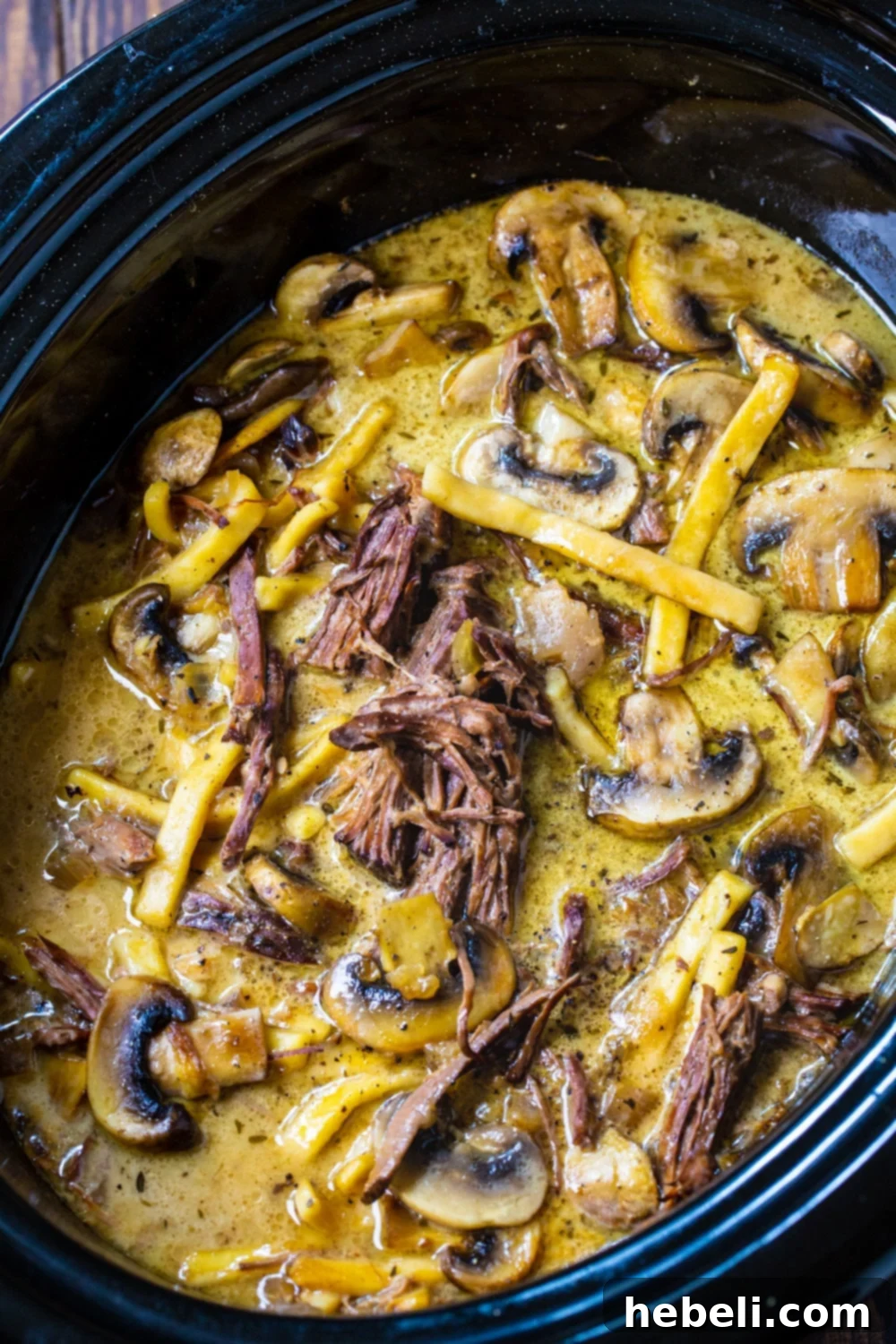 Slow Cooker Beef and Noodles with Mushrooms simmering in a crock pot, nearly ready.