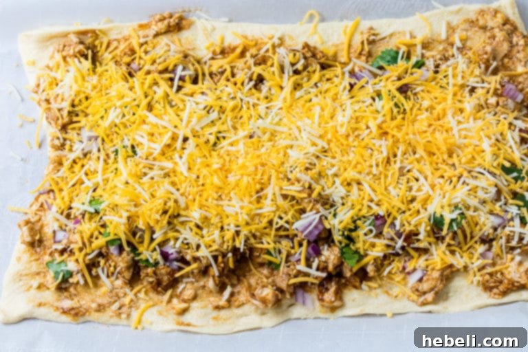 Sprinkling shredded Colby Jack cheese over the BBQ chicken and onion mixture on crescent dough.