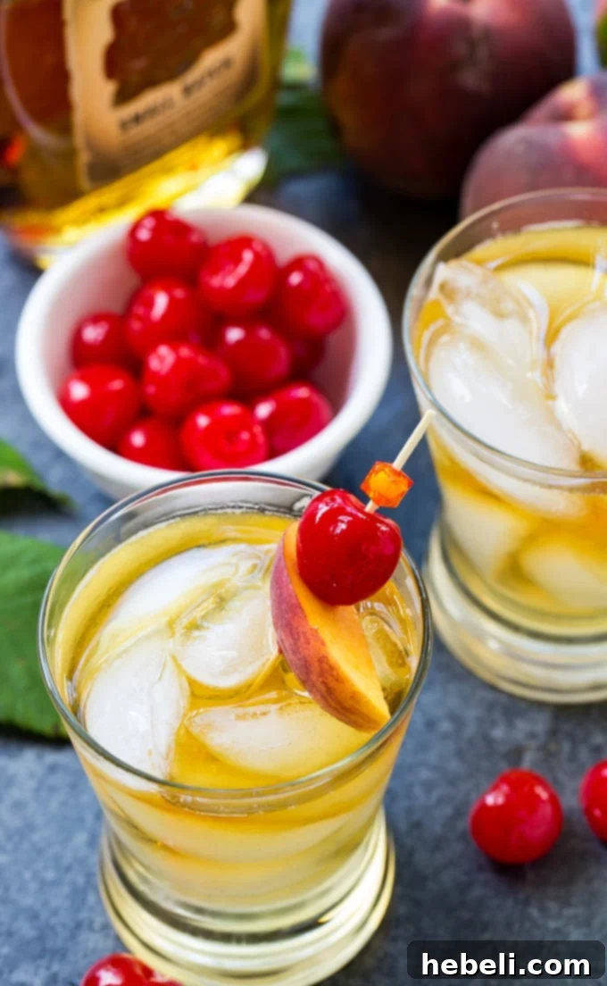 Close-up of a Peach Old-Fashioned cocktail with a bourbon bottle in the background.