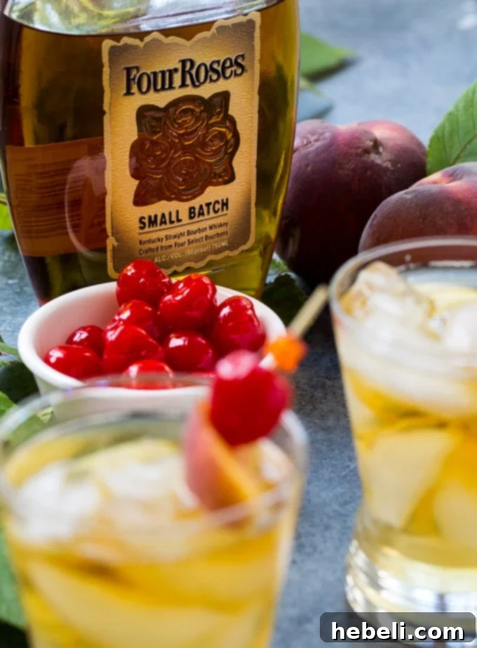 A Peach Old-Fashioned cocktail garnished with a peach slice and orange peel, alongside a bottle of Four Roses bourbon.