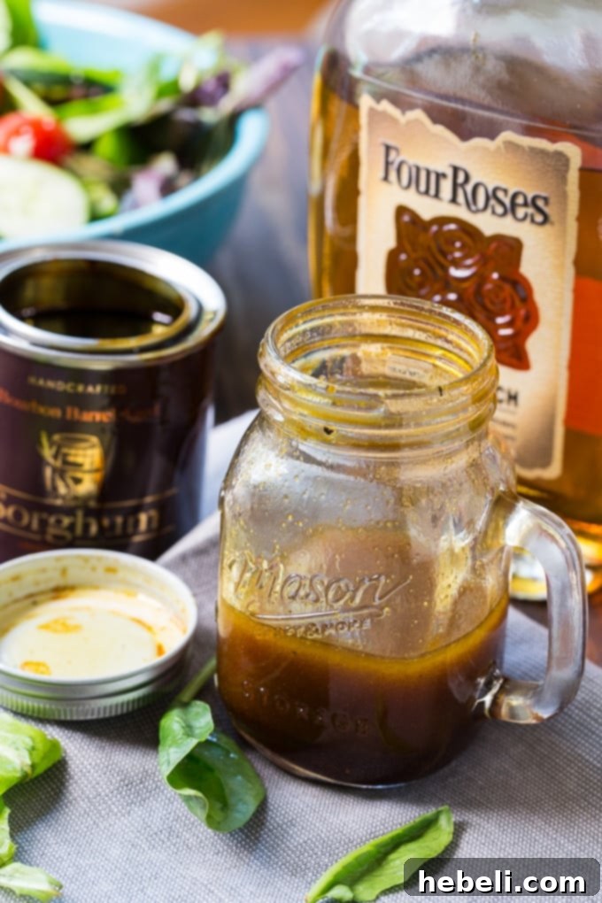 Golden Bourbon Sorghum Dressing 3 Bourbon Sorghum Vinaigrette in a glass cruet, next to a bottle of Four Roses Bourbon, highlighting its key ingredient and Southern origins.