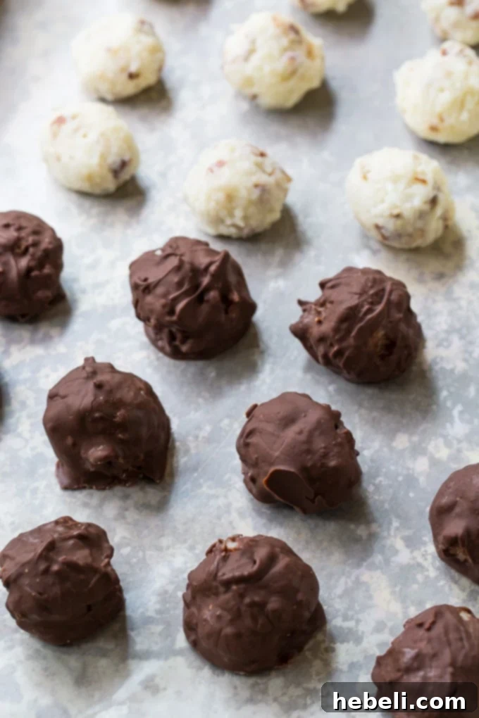 A baking sheet filled with perfectly shaped Martha Washington Candy balls, some already dipped in chocolate and others awaiting their turn, highlighting the contrasting textures and preparation stages.