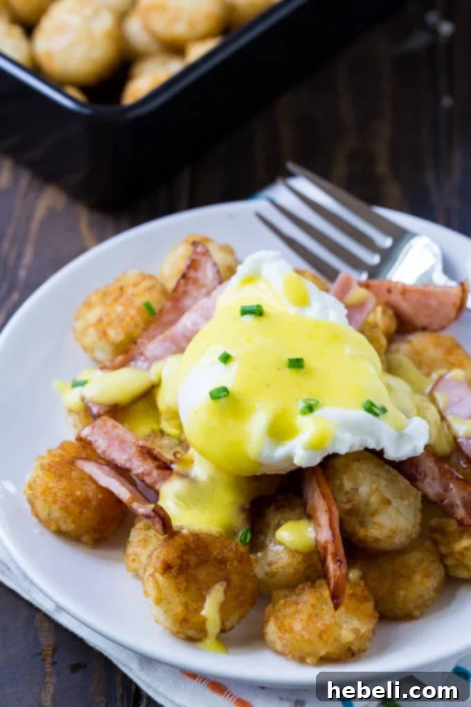 Golden Tater Tot Benedict 3 Close-up of Tater Tot Eggs Benedict on a crispy bed of tater tots with Canadian bacon, showcasing the runny yolk and Hollandaise sauce.
