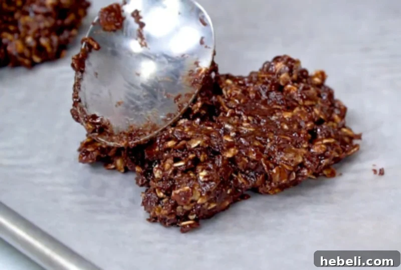 A spoonful of chocolate oatmeal cookie mixture being dropped onto parchment paper to form a cookie.