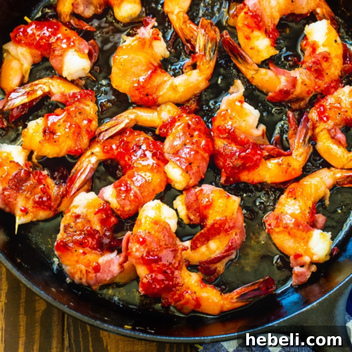 Bacon-Wrapped Shrimp with Pepper Jelly Glaze glistening in a cast iron pan.