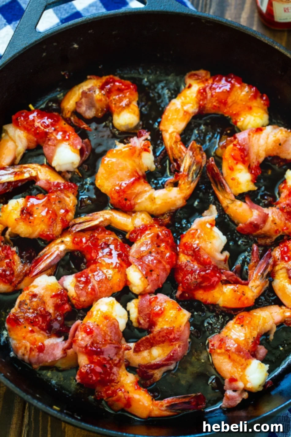 Shrimp wrapped in bacon cooking in a cast iron pan, ready for the glaze.