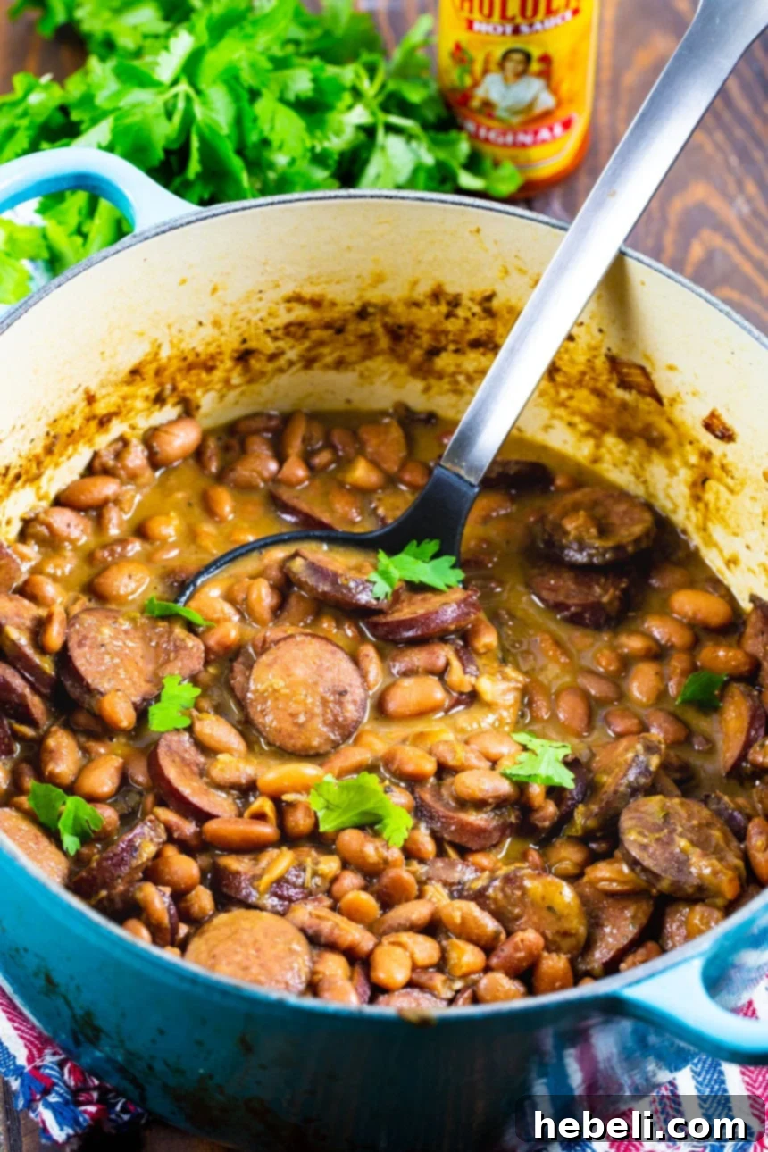 Spoon scooping up creamy, tender Pintos and Sausage from a bowl.