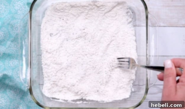 Smothered Steak Bites with Golden Onion Gravy 4 A shallow dish containing a mixture of white flour, garlic salt, and black pepper, ready for dredging.