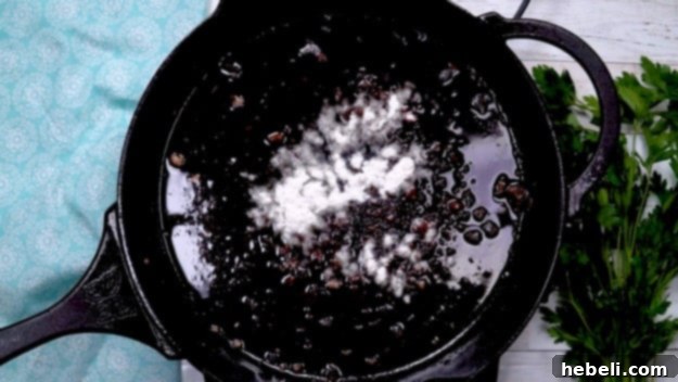 Smothered Steak Bites with Golden Onion Gravy 7 A small amount of flour being added to pan drippings in a skillet, creating a light brown roux for gravy.