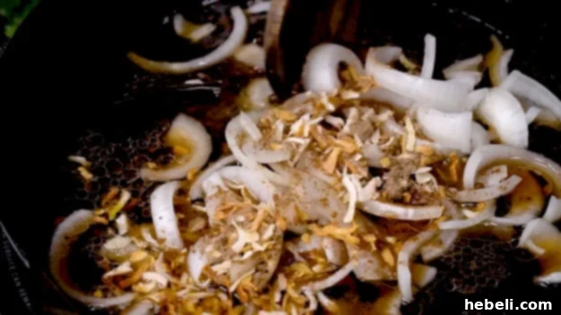 Smothered Steak Bites with Golden Onion Gravy 8 Sliced onions, beef broth, and a packet of dry onion soup mix being added to a skillet with pan drippings, stirring to combine.