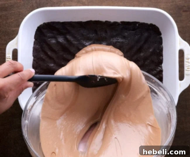 Spreading the Nutella cream cheese filling over the chocolate cake crust in a baking pan.