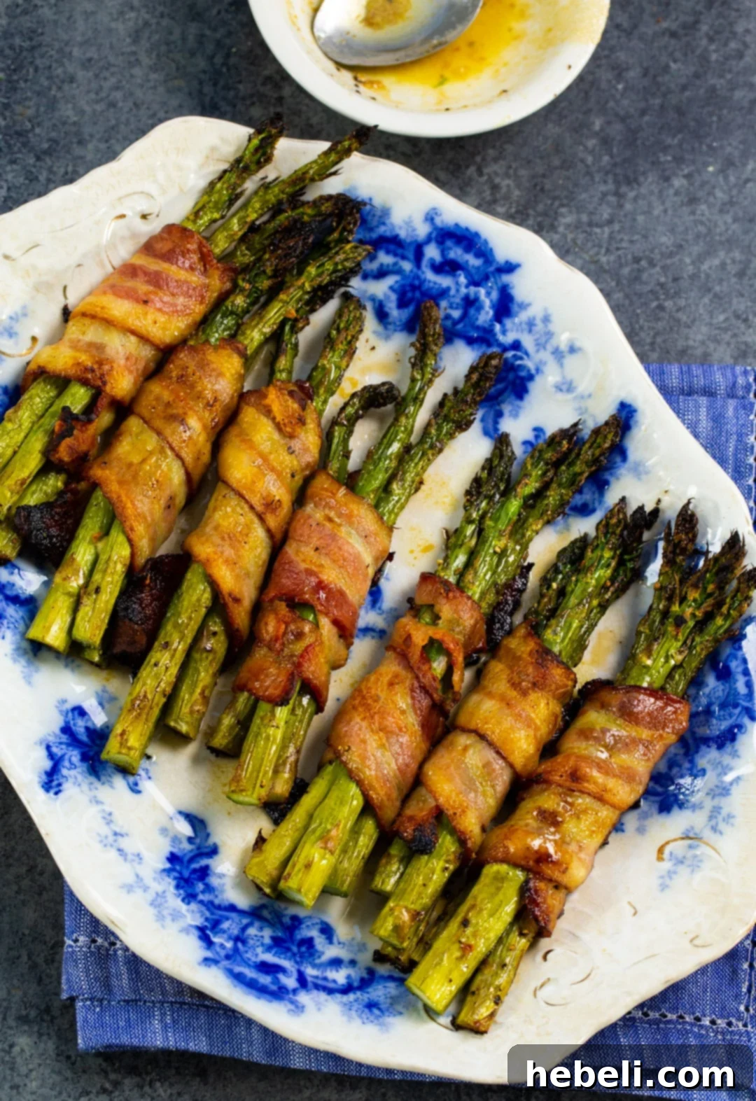 Asparagus Bundles wrapped with strips of bacon, neatly arranged on a plate before cooking.