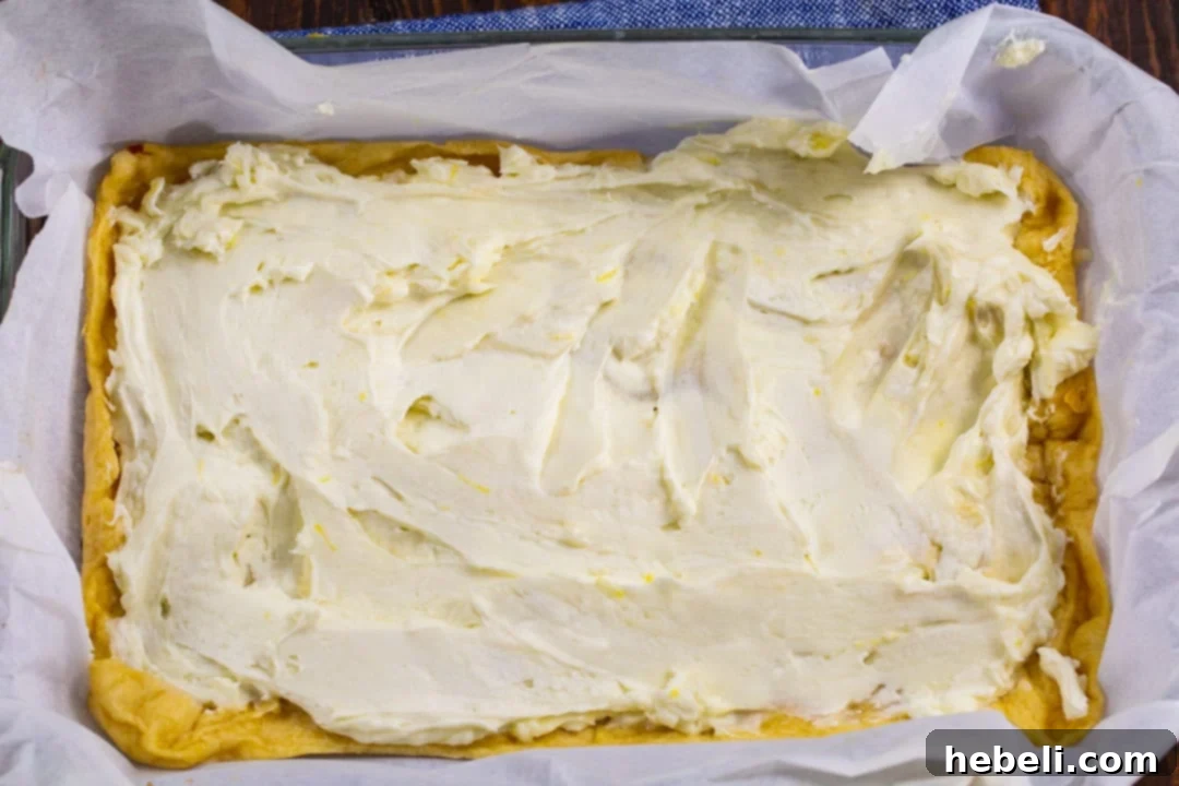 Zesty Lemon Cream Cheese Bars 4 Smooth cream cheese mixture evenly spread across the pre-baked crescent dough crust, creating a luscious layer.