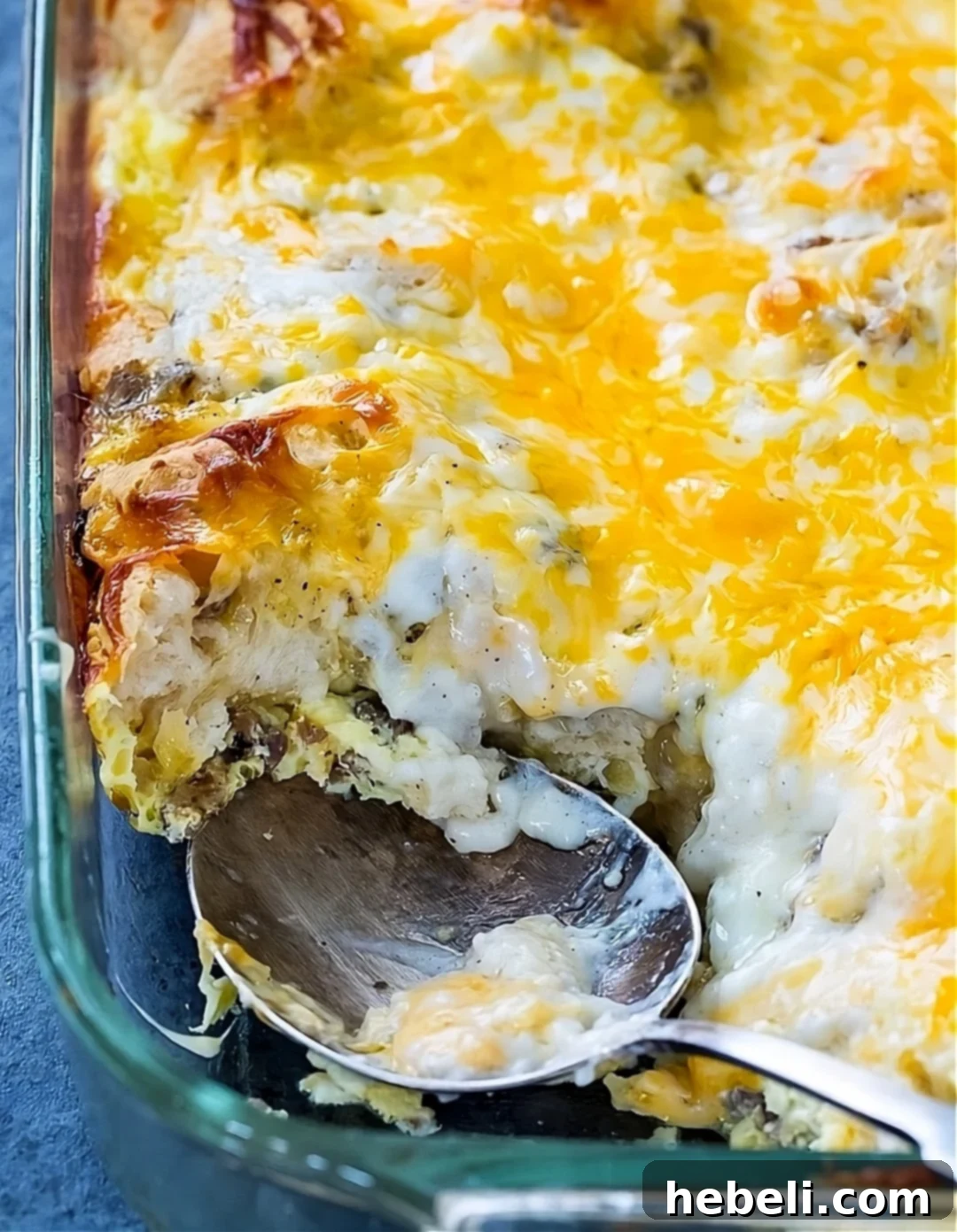 A serving spoon scoops into a freshly baked Biscuits and Gravy Casserole, revealing layers of golden biscuits, rich sausage gravy, scrambled eggs, and melted cheese.