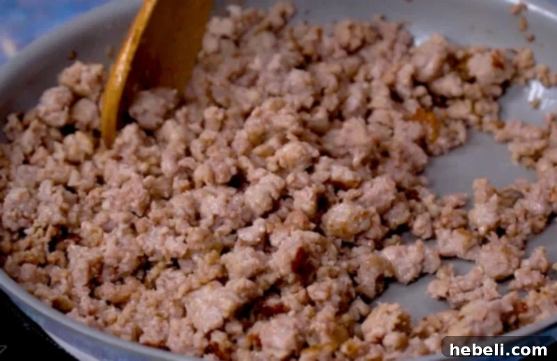 Crumbled breakfast sausage browning in a large skillet, releasing its savory aroma.