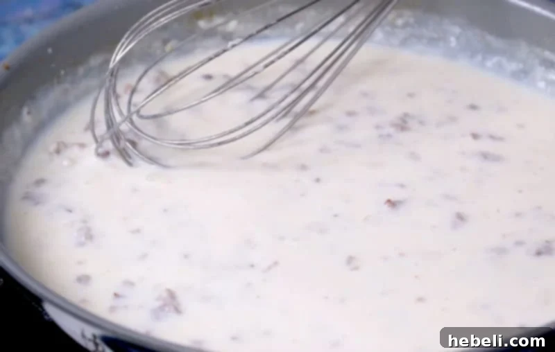 Thick, creamy sausage gravy simmering in a pan, with a whisk stirring the mixture.