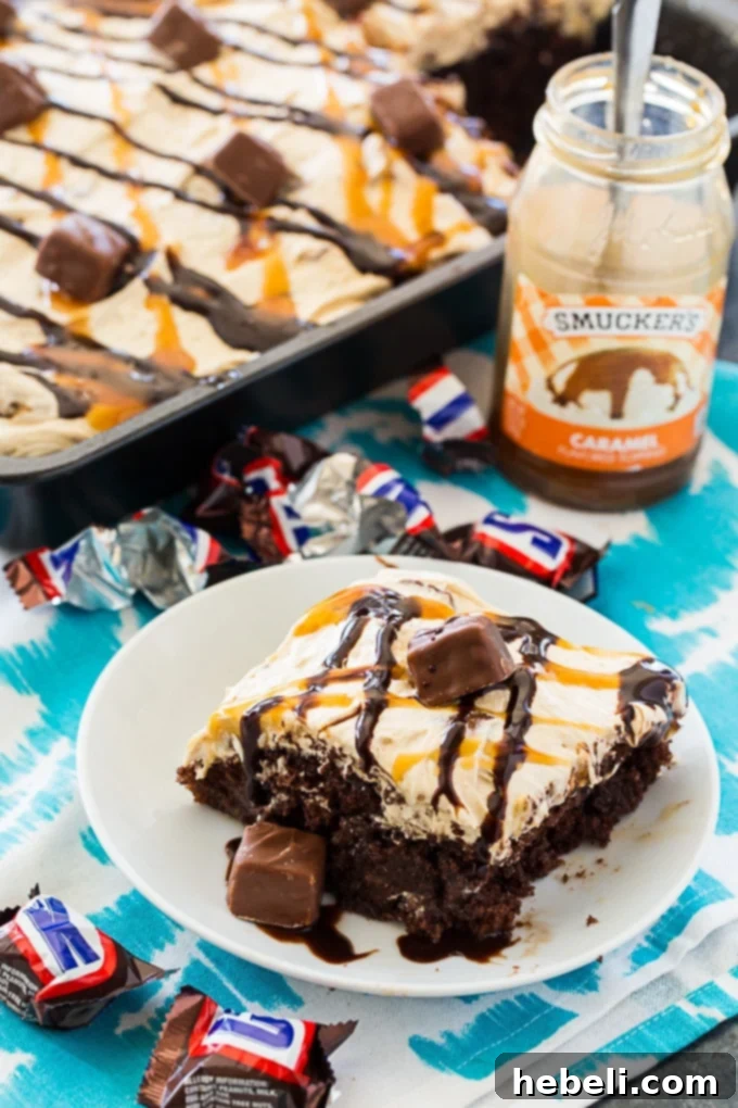 A close-up view of the Snickers Poke Cake with its rich peanut butter frosting, sprinkled with chopped peanuts and a swirl of caramel, highlighting its decadent layers.