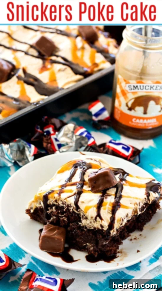 A large serving of Snickers Poke Cake in a baking pan, showing the thick layer of peanut butter frosting and an abundance of chopped candy bars on top.