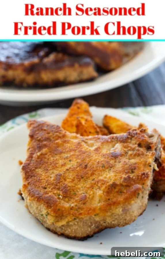 Two Ranch Seasoned Fried Pork Chops on a plate, ready to be served, garnished with fresh herbs and a delicious side dish