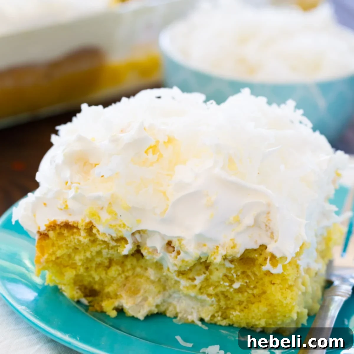 A delectable slice of Coconut Cream Poke Cake on a vibrant blue plate, showcasing its moist texture and rich layers of whipped topping and shredded coconut.