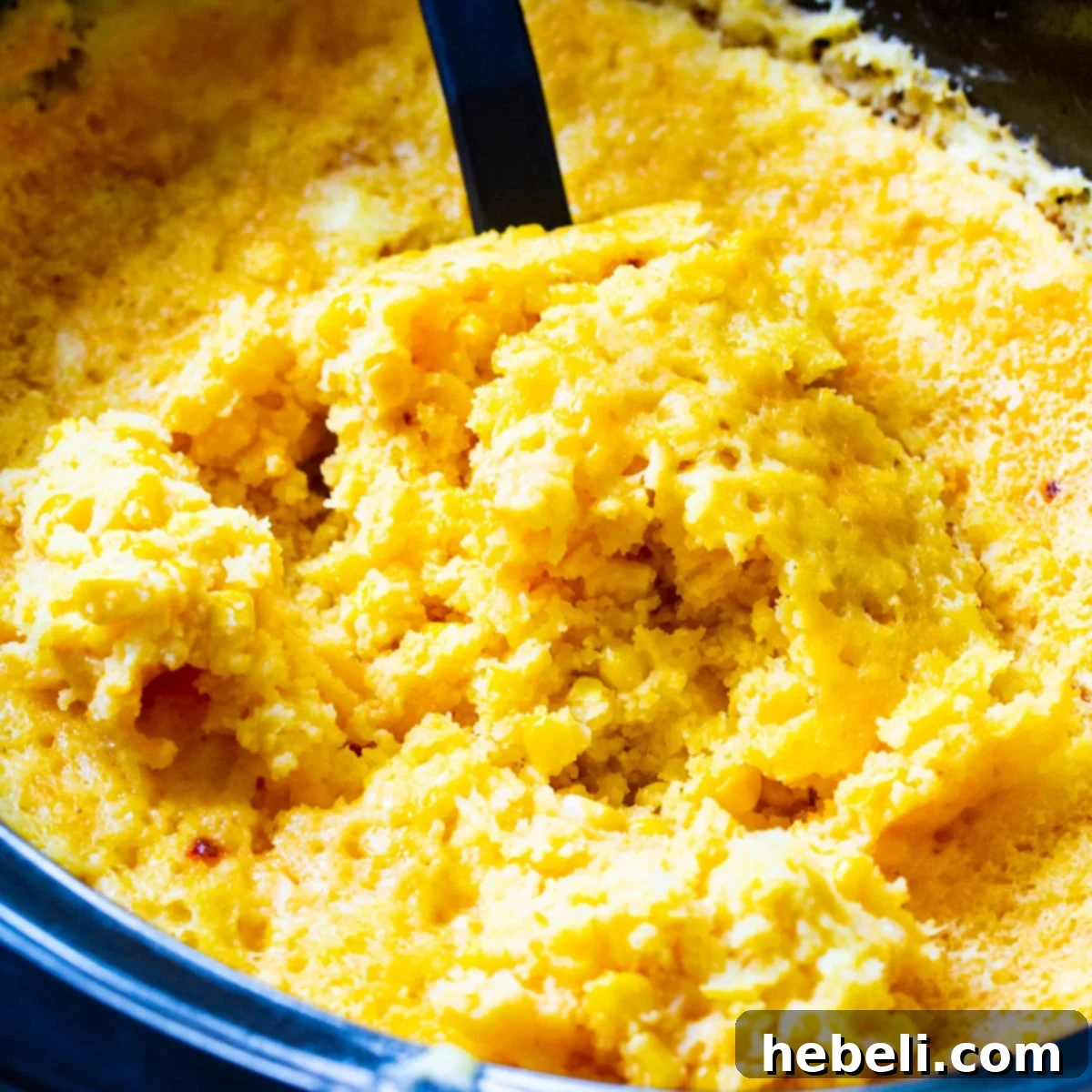A spoon scooping a generous portion of creamy Crock Pot Corn Casserole from a slow cooker, showcasing its golden-brown top and rich, enticing texture.