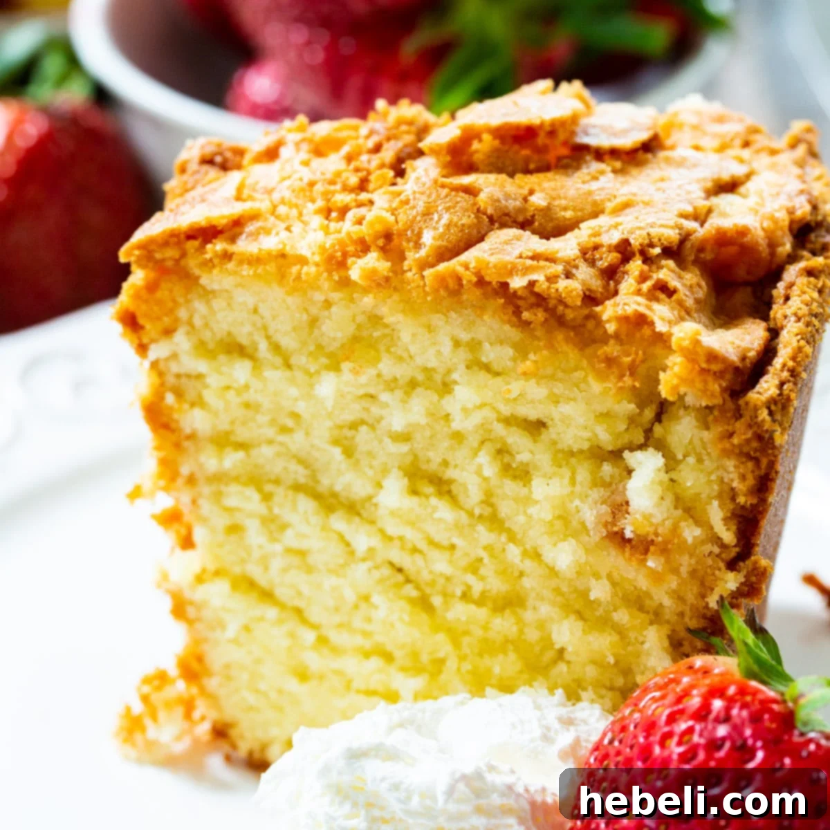Slice of Classic Southern Pound Cake with whipped cream and a strawberry, highlighting its moist texture.