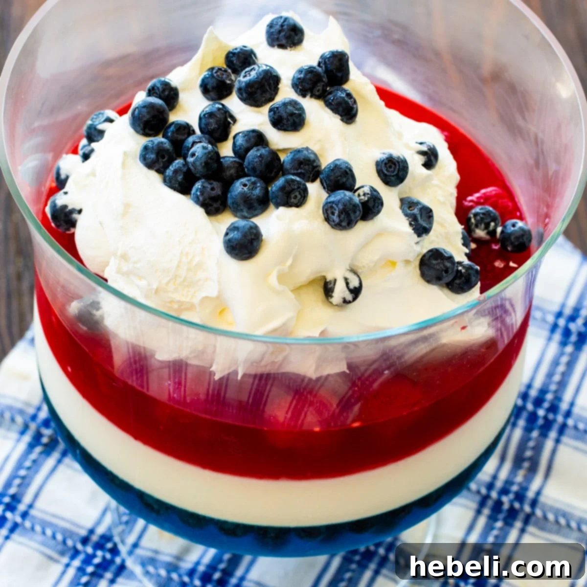 Festive Red White and Blue Jello 2 A visually stunning Red, White & Blue Jello Salad in a clear trifle bowl, showcasing distinct patriotic layers of blue gelatin with blueberries, a creamy white layer, and red gelatin with raspberries. It's a perfect dessert for 4th of July festivities.