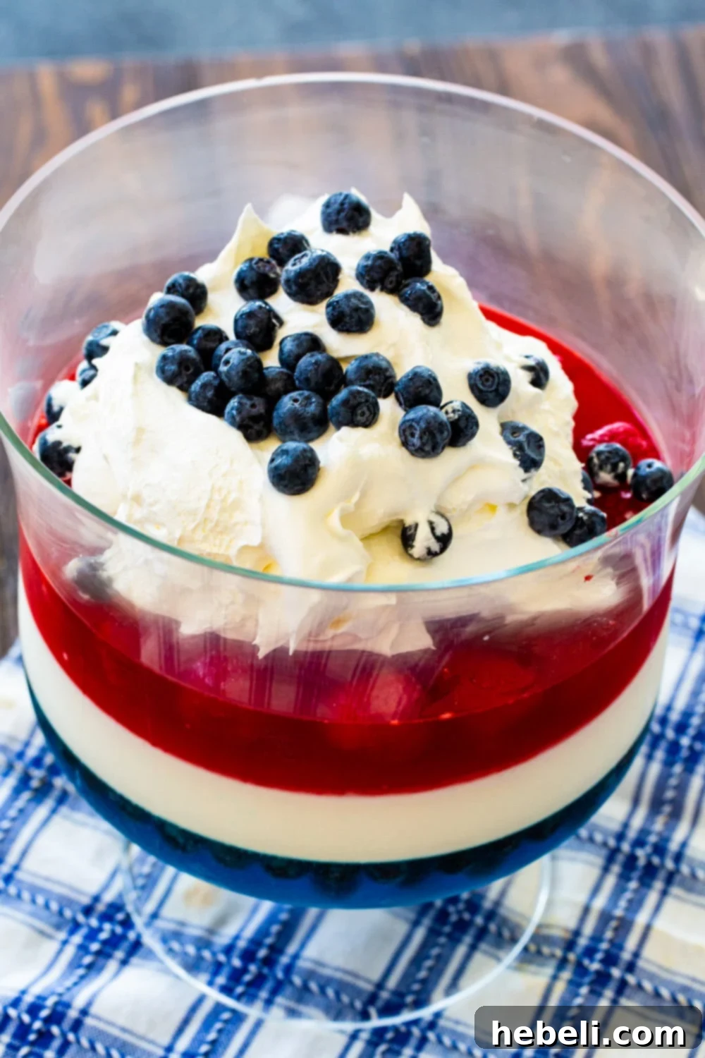 Festive Red White and Blue Jello 3 A close-up of the Red, White & Blue Jello Salad in a trifle bowl, topped with a generous swirl of whipped cream and garnished with fresh blueberries, ready for serving at a patriotic event like the 4th of July.
