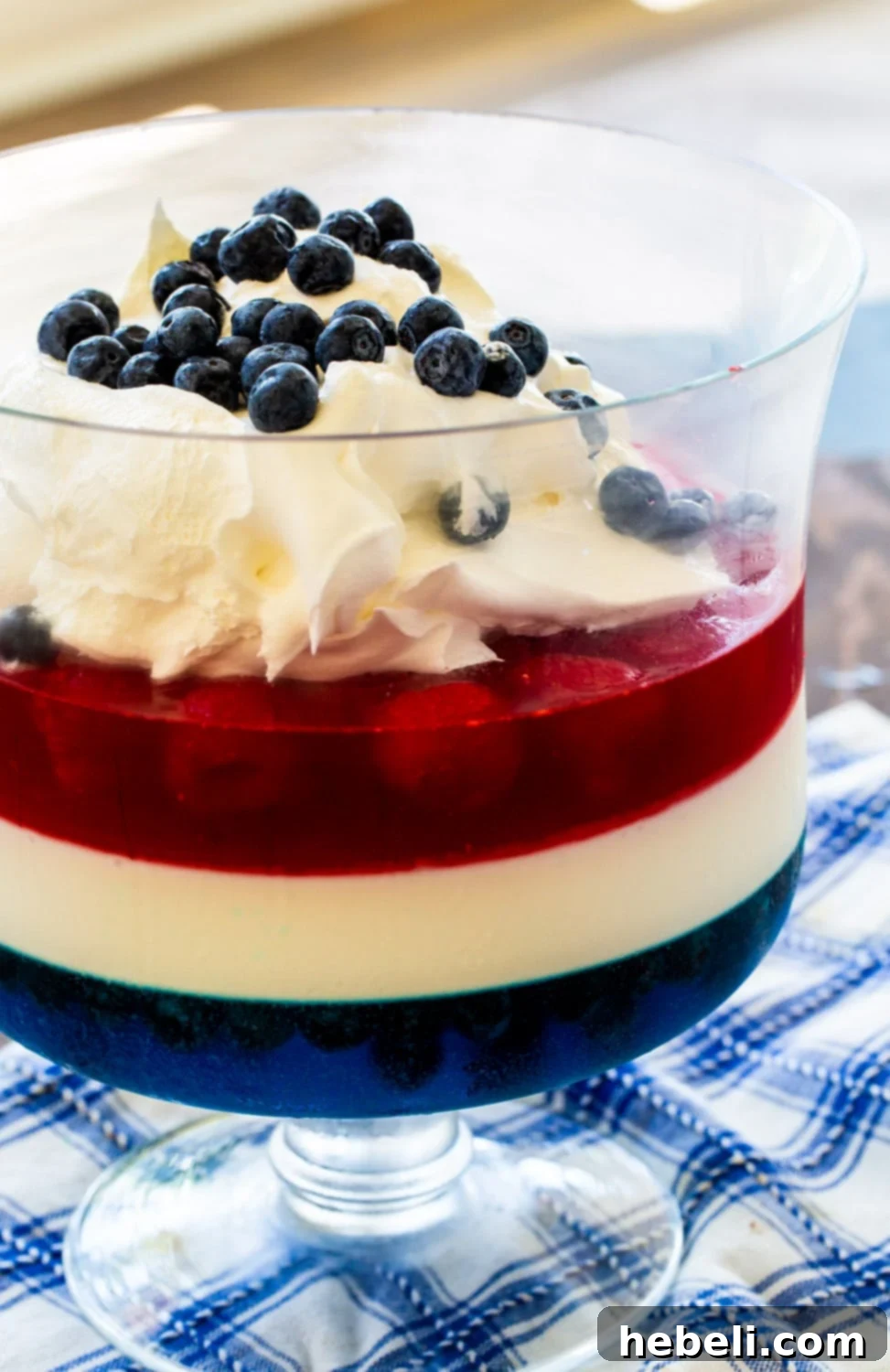 Festive Red White and Blue Jello 4 The Red, White & Blue Jello Salad is expertly garnished with a dollop of whipped cream and fresh blueberries, ready to be served. The distinct layers are visible and appealing.
