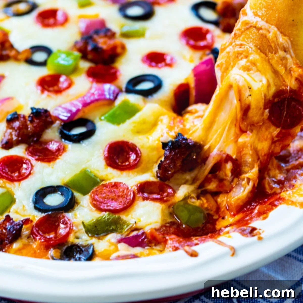 A breadstick generously scooping a portion of Supreme Pizza Dip, showcasing its melted cheese, pepperoni, sausage, and colorful vegetable toppings.