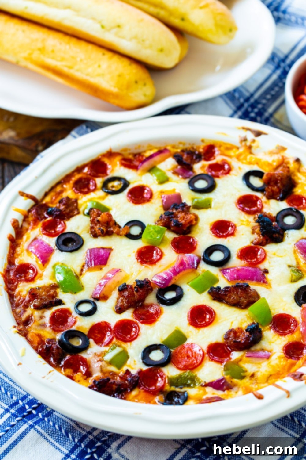 A piping hot Supreme Pizza Dip served with a plate of golden breadsticks, ready for dipping. Shows melted cheese and abundant toppings.