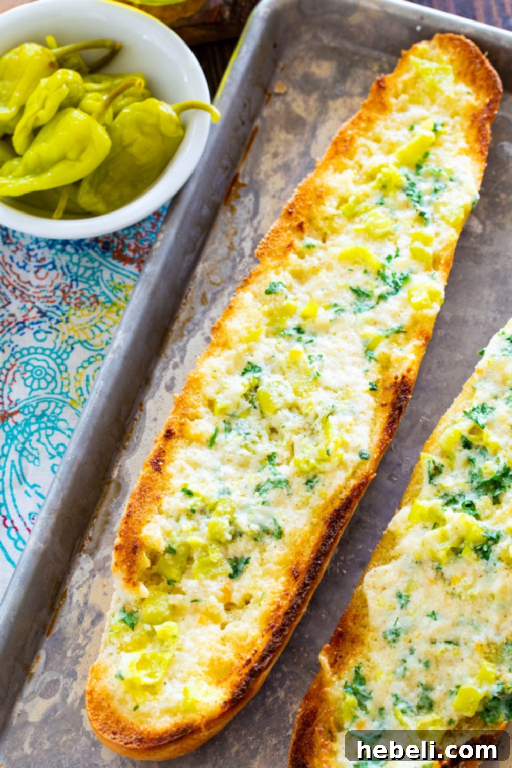 A full loaf of Pepperoncini Garlic Bread next to a small bowl of whole pepperoncini peppers.