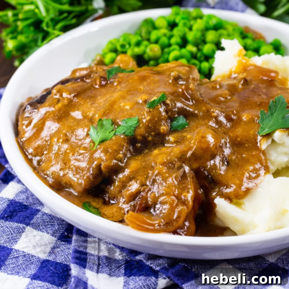 Crock Pot Cubed Steak with Gravy on a plate with mashed potatoes and peas.