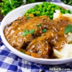 Crock Pot Cubed Steak with Gravy on a plate with mashed potatoes and peas.