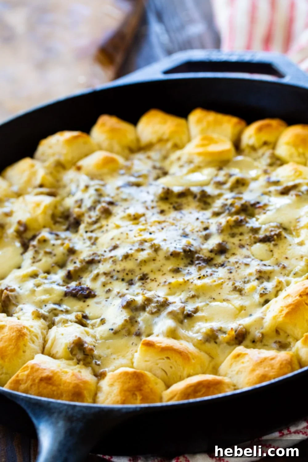 Sausage gravy surrounded by uncooked biscuit dough in a cast iron pan, ready for baking.