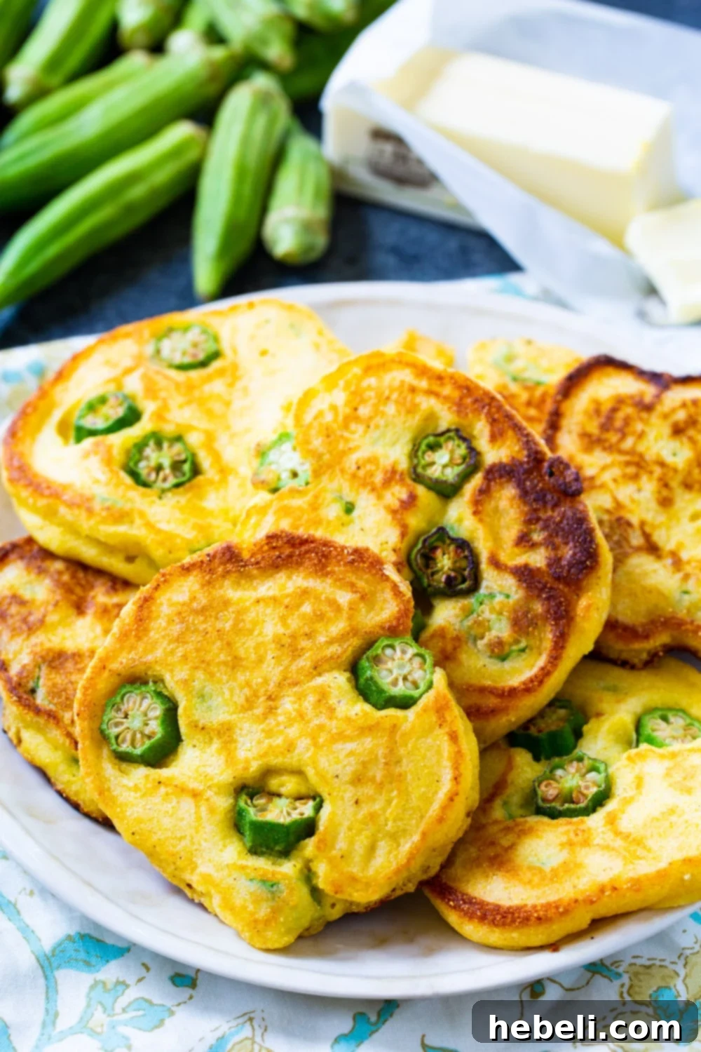 Crispy Okra Hoecakes 3 Close-up of golden brown Okra Hoecakes on a plate with fresh okra pods in the background.