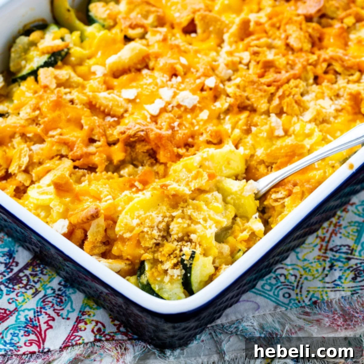 Spoon scooping a generous portion of Cheesy Squash, Zucchini, and Corn Casserole from a baking dish, showcasing its creamy texture and golden-brown topping.