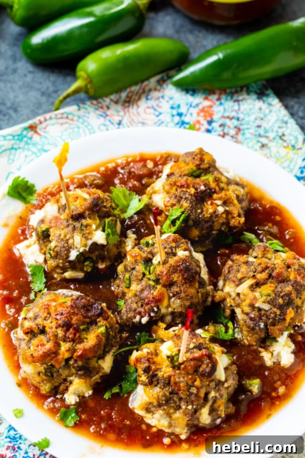 Plate full of Golden Brown Jalapeno Popper Meatballs with fresh jalapenos next to it, highlighting their key ingredient.