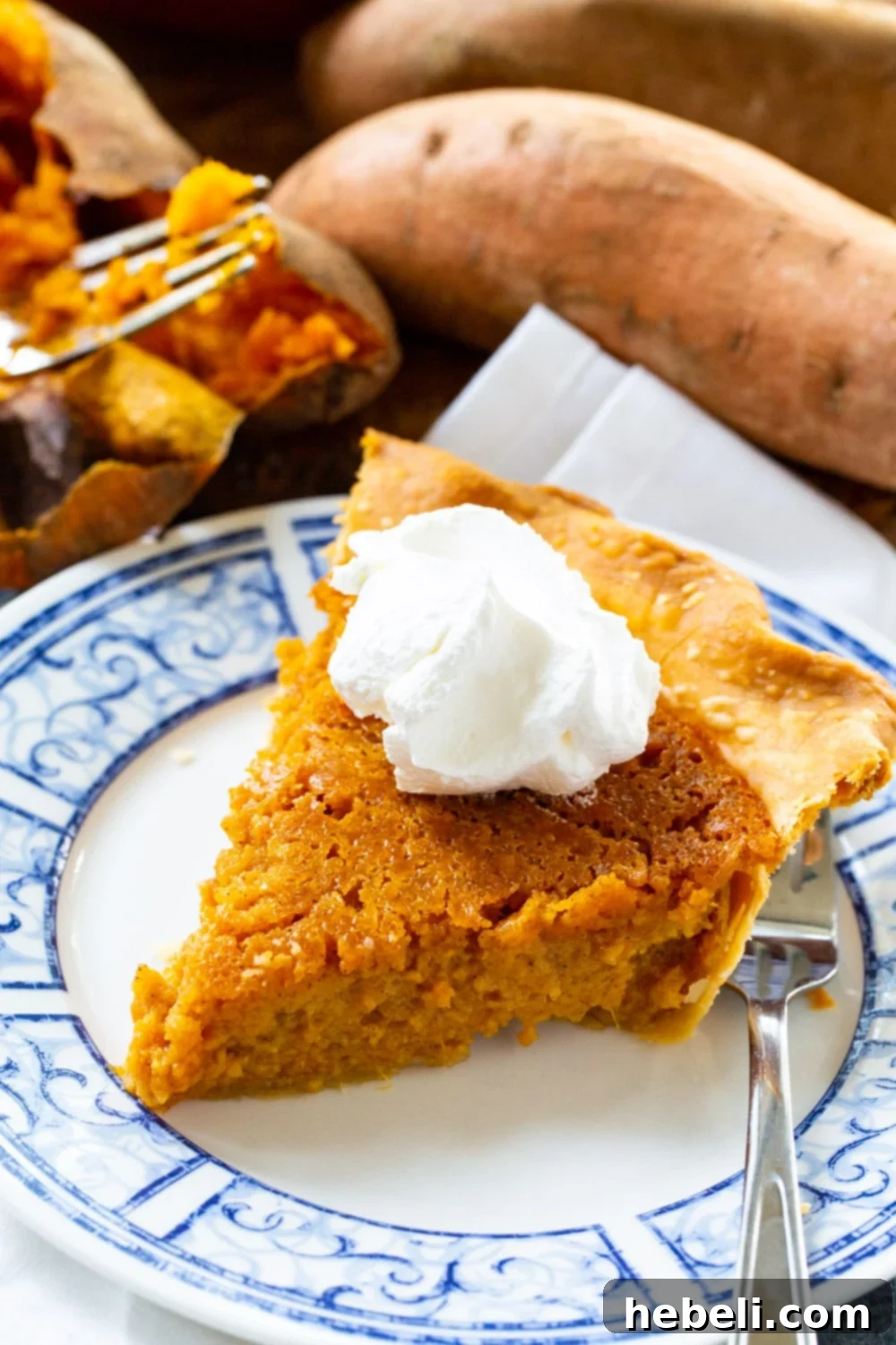 Slice of sweet potato pie on a plate with fresh sweet potatoes and fall leaves in the background, highlighting the seasonal delight.