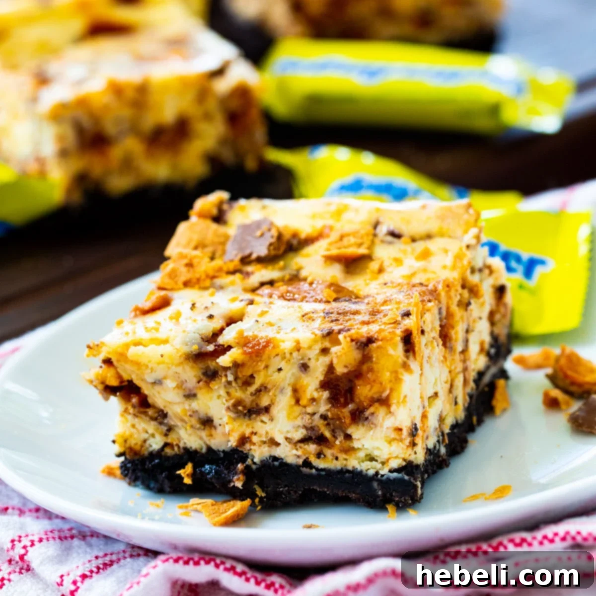 Decadent Butterfinger Cheesecake Bars 2 Delicious Butterfinger Cheesecake Bars on a serving plate, showcasing the chocolate Oreo crust and creamy filling with candy bits.