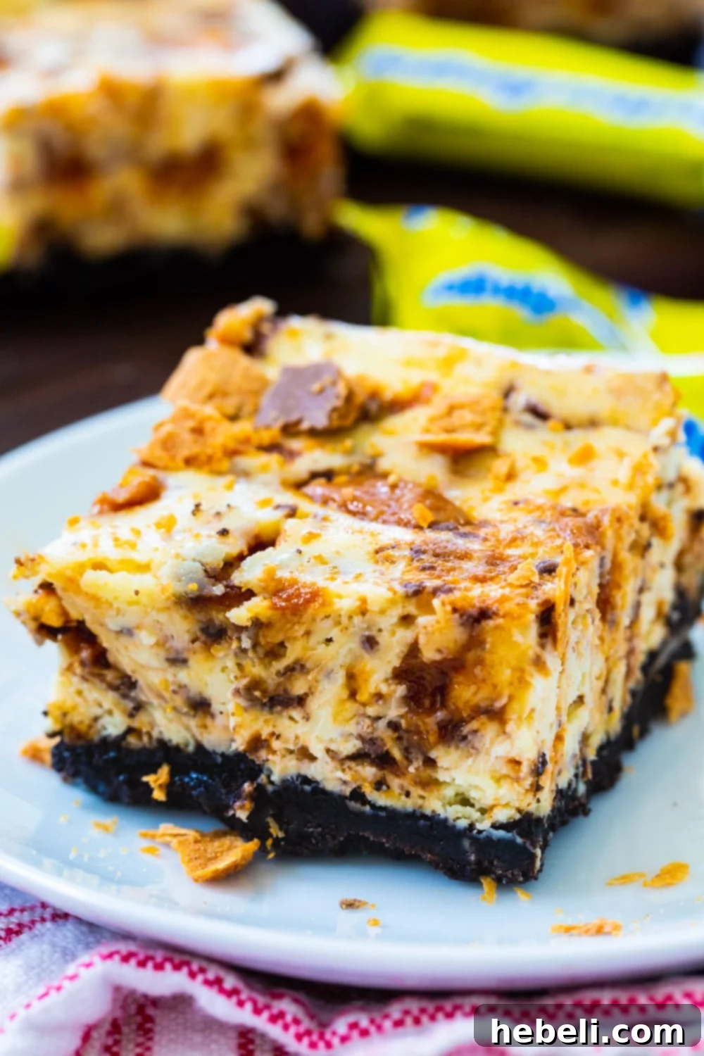 Decadent Butterfinger Cheesecake Bars 4 A single Butterfinger Cheesecake Bar on a small white plate, surrounded by mini Butterfinger candies, highlighting the crunchy candy pieces.