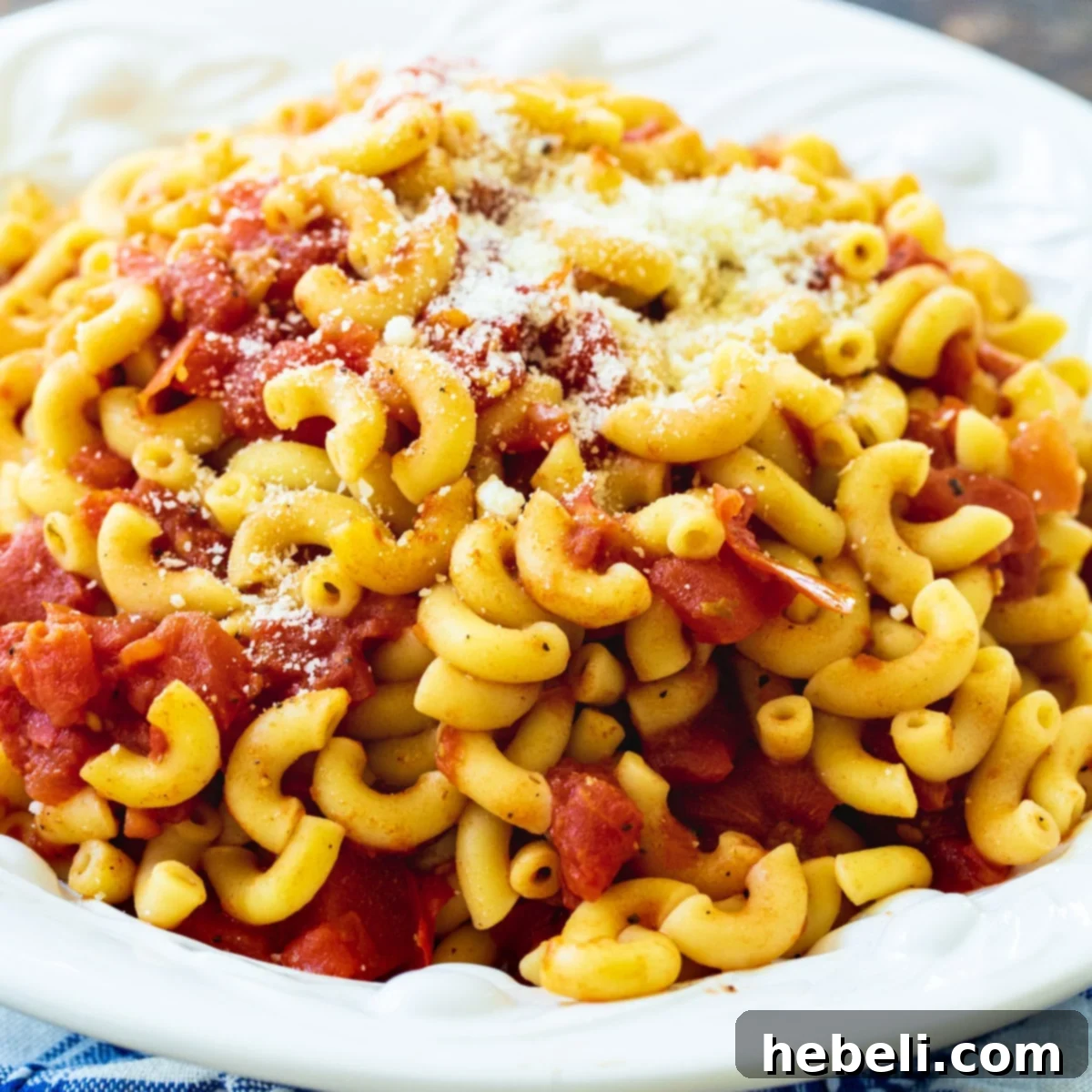 A steaming bowl of Macaroni and Tomatoes, generously topped with freshly grated Parmesan cheese, showcasing its rich, red sauce and tender elbow macaroni.
