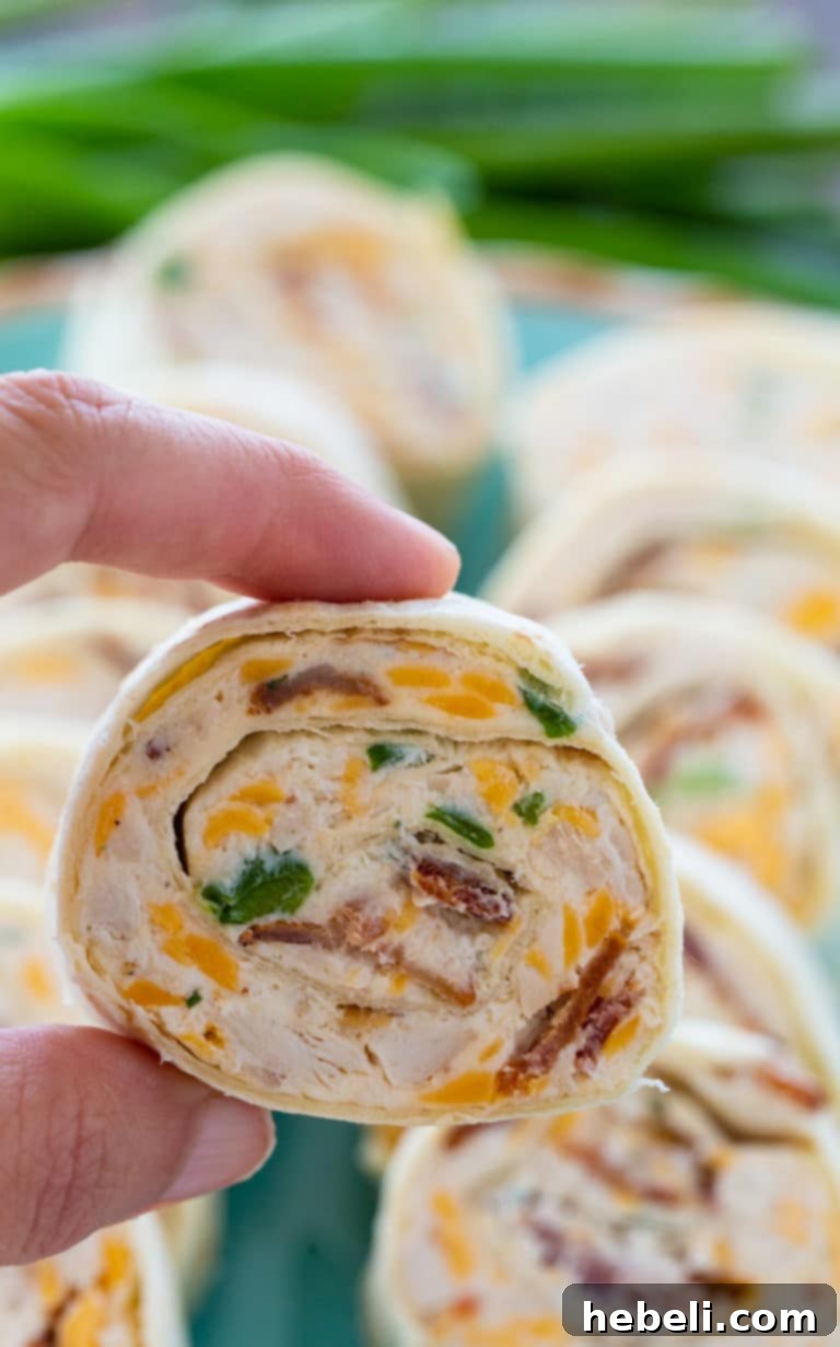 Stacked Chicken, Bacon, and Cheddar Pinwheels on a white plate, emphasizing their appeal as an easy and delicious party appetizer.