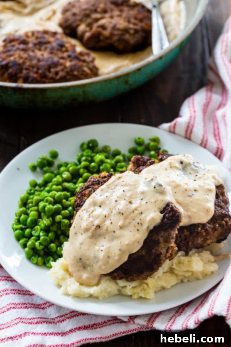 Close-up of a skillet filled with golden-brown Hamburger Steaks, generously smothered in a rich, creamy white Country Gravy, ready to be served.