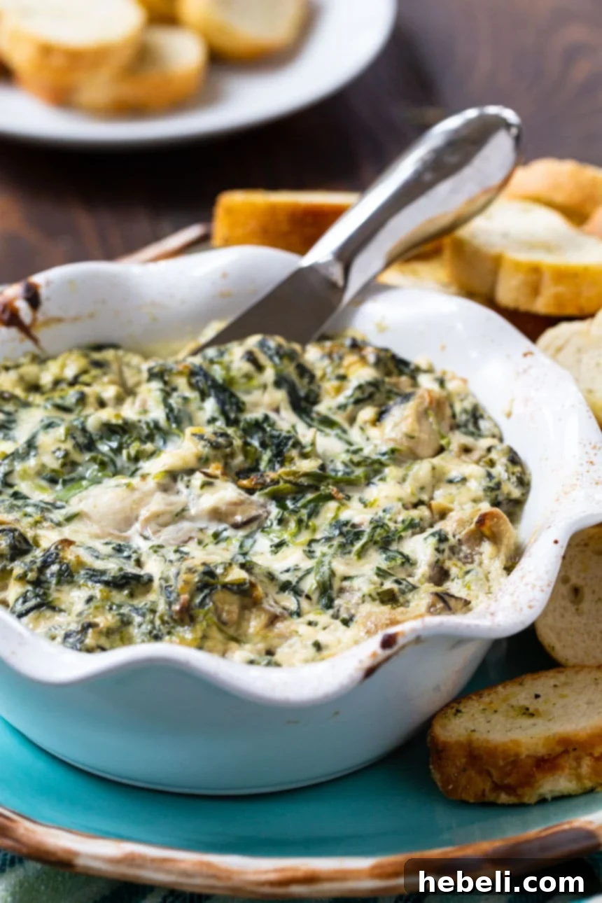 Oysters Rockefeller Dip served warm in a ceramic dish, surrounded by golden toasted baguette slices for dipping.