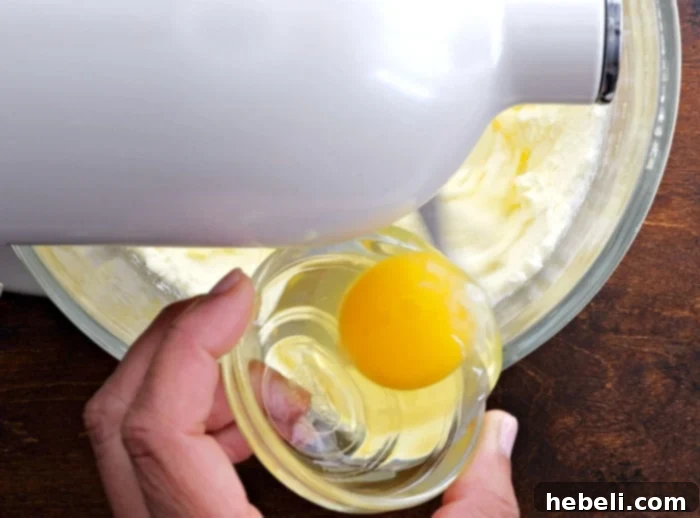 Eggs being added one by one to the creamed butter and sugar mixture.