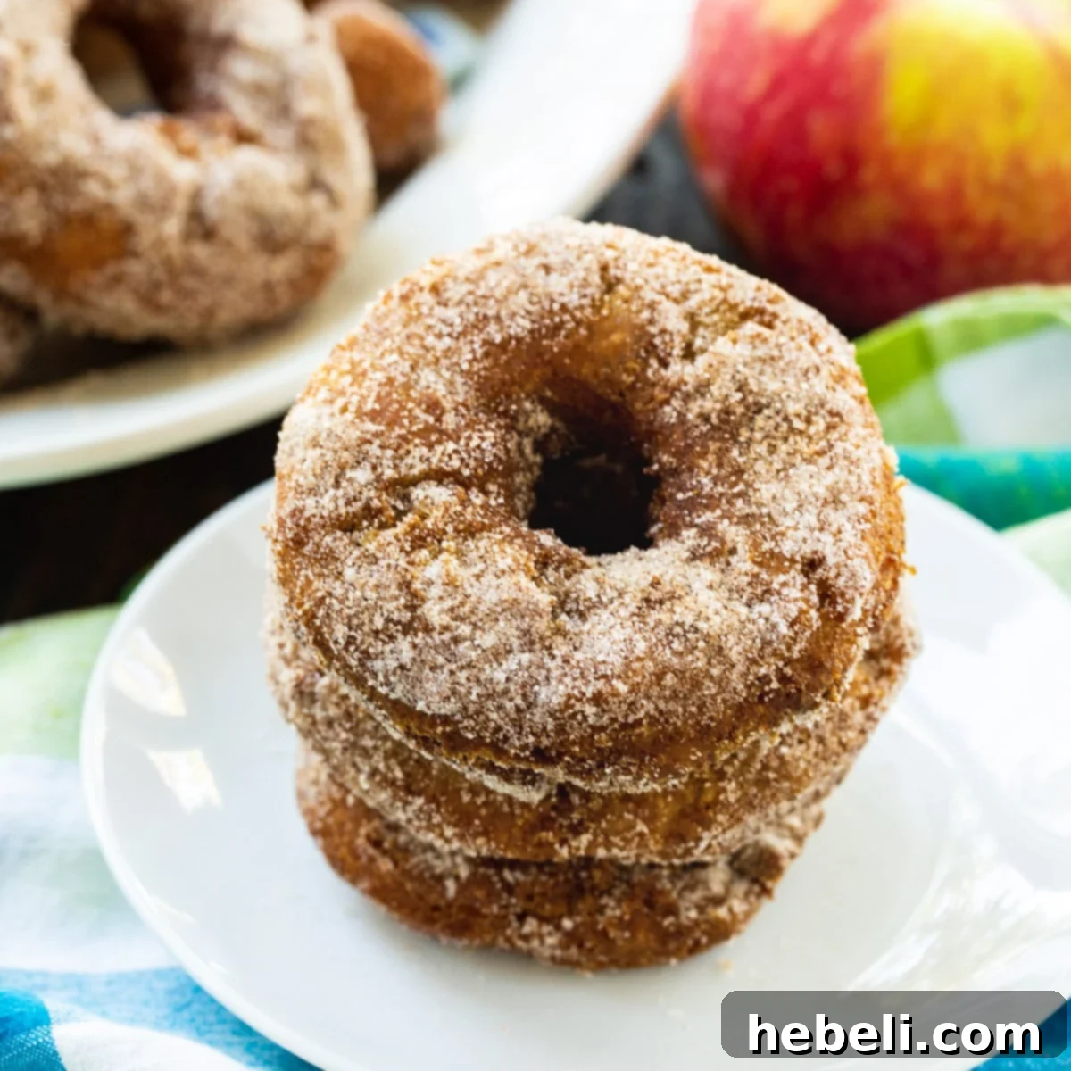 Stacked Apple Cider Doughnuts on a plate, generously coated in cinnamon-sugar, embodying a cozy autumn theme.
